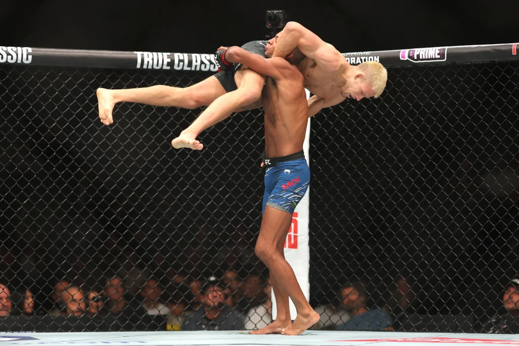 UFC 320: Patchy Mix - Jakub Wikłacz Zawodnik podnosi swojego przeciwnika nad ramiona podczas walki MMA w oktagonie, wokół widoczna publiczność i ogrodzenie ringu.