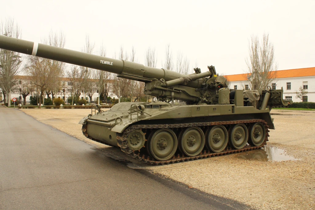 Haubica samobieżna M110. Mogła wystrzeliwać specjalne pociski z ładunkiem nuklearnym o mocy do 40 kiloton Ciężka armata samobieżna na gąsienicowym podwoziu stoi zaparkowana na utwardzonym placu, w tle budynki koszarowe i rząd bezlistnych drzew.