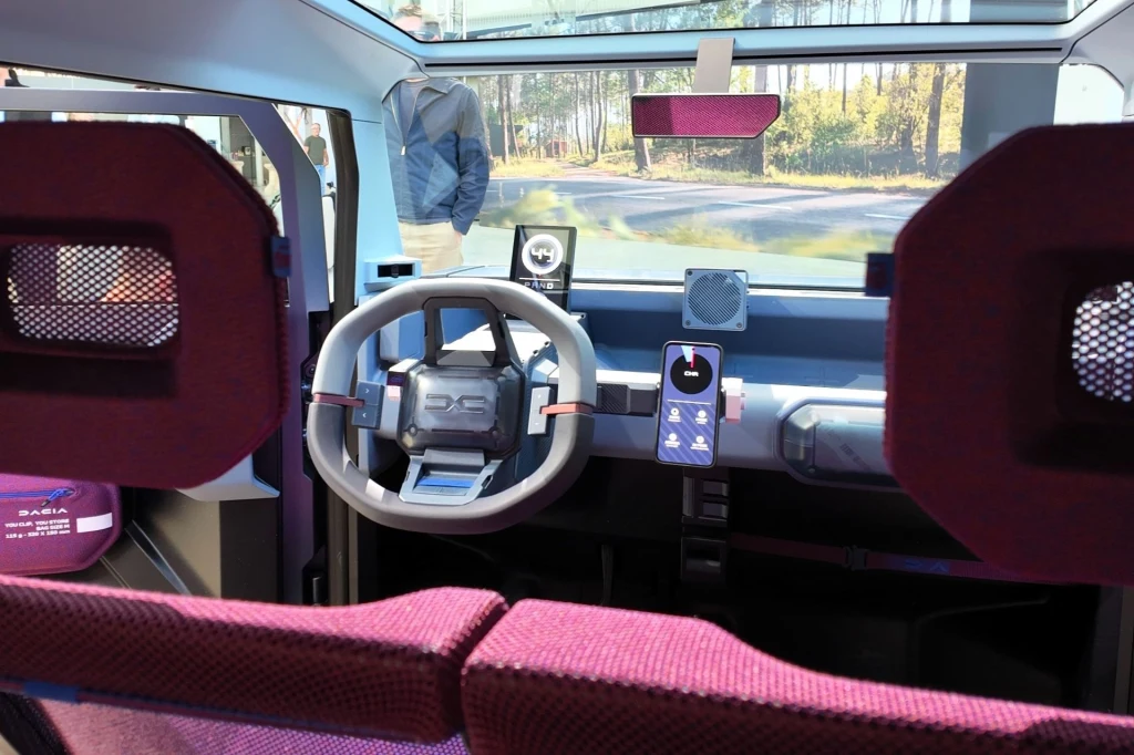 Mimo stosunkowo niewielkich rozmiarów wnętrze Dacii Hipster Concept jest zaskakująco przestronne i pomieści cztery dorosłe osoby. Futurystyczne wnętrze samochodu z geometryczną kierownicą, nowoczesnymi panelami sterowania i panoramiczną szybą, siedzenia obite bordową tapicerką, za szybą widoczne drzewa.