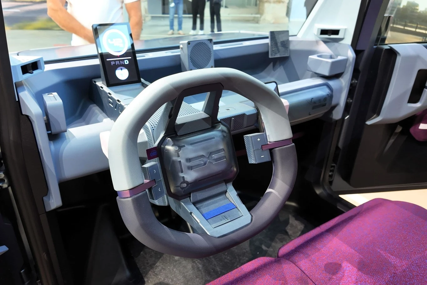 Wnętrze Dacii Hipster Concept wyposażone jest tylko w najpotrzebniejsze elementy. Auto można jednak doposażyć o akcesoria YouClip. Przygotowano 11 punktów mocowania. Nowoczesna deska rozdzielcza samochodu elektrycznego z futurystyczną kierownicą o geometrycznym kształcie, cyfrowym wyświetlaczem i fioletowym fotelem, w tle widoczne są detale technologiczne oraz fragmenty nadwozia.