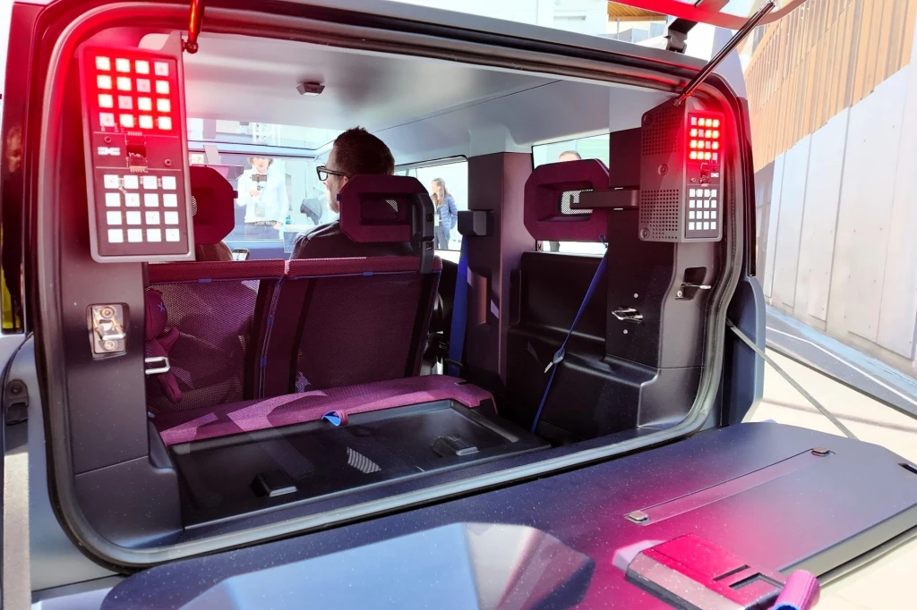 Bagażnik Dacii Hipster Concept pomieści 70 litrów. Po złożeniu tylnych siedzeń przestrzeń ta rośnie do 500 litrów. Widok wnętrza futurystycznego pojazdu, z otwartą tylną klapą, nowoczesnymi panelami kontrolnymi z czerwonymi podświetleniami oraz pasażerami widocznymi przez szybę, siedzącymi na przednich fotelach.