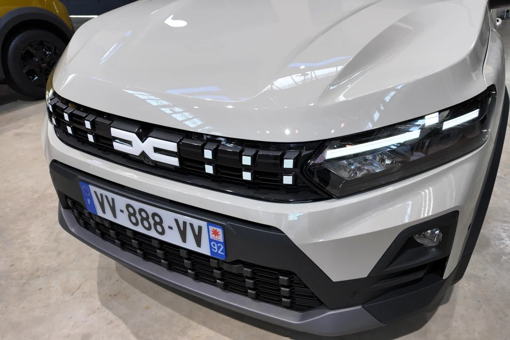 Po modernizacji Dacia Jogger i Sandero (w tym Sandero Stepway) zostały wyposażone w nową osłonę chłodnicy i światła do jazdy dziennej w kształcie odwróconej litery "T". Nowoczesny przód białego samochodu z czarnym grillem i stylizowanymi światłami LED, oznaczony francuską tablicą rejestracyjną VV-888-VV.