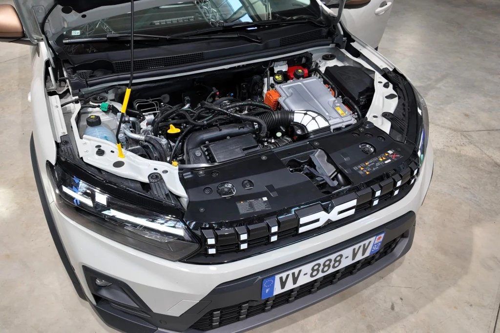 W Dacii Jogger, a od czwartego kwartału 2026 r. także w Sandero Stepway, pojawi się nowy układ hybrydowy generujący 155 KM i 205 Nm. Otwarta maska samochodu ukazująca szczegóły silnika i elementów pod maską, widoczne logo marki Dacia oraz tablica rejestracyjna z numerem VV-888-VV.