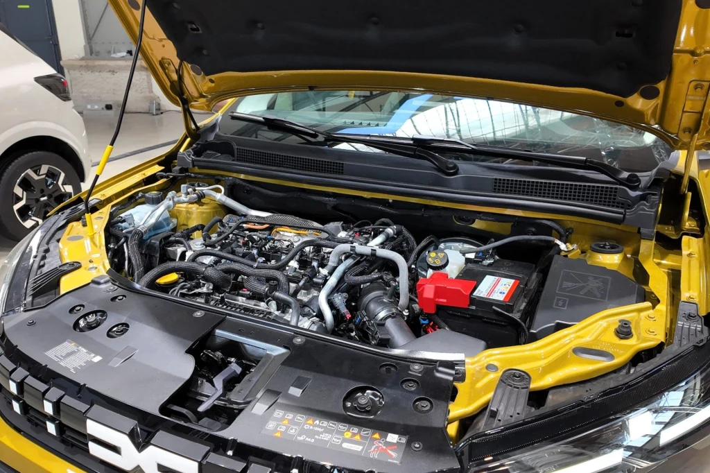 Nowością w obu wariantach Sandero oraz w Joggerze będzie trzycylindrowy turbodoładowany silnik 1,2 generujący 120 KM i 200 Nm. Współpracować on będzie z instalacją LPG. Otwarta maska żółtego samochodu odsłaniająca nowoczesny silnik z licznymi przewodami, częściami elektronicznymi oraz akumulatorem z wyraźnie oznakowanymi elementami bezpieczeństwa.