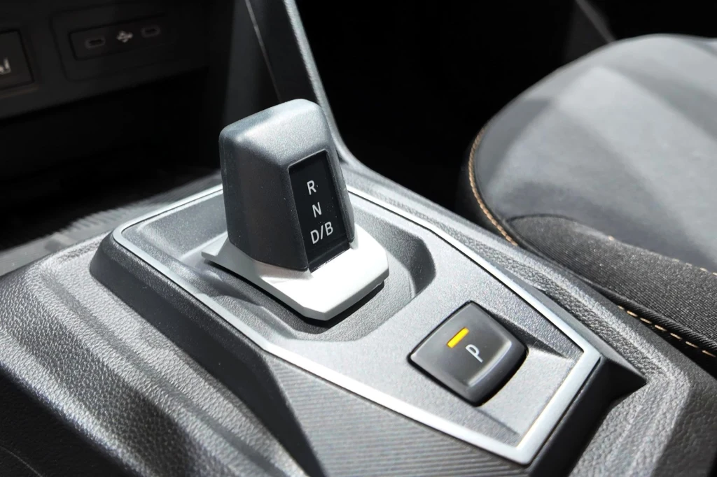 W ramach modernizacji Dacii Sandero i Jogger skrzynia automatyczna została wyposażona w nową dźwignię. Panel środkowy samochodu z nowoczesną dźwignią zmiany biegów automatycznej skrzyni, obok widoczny przycisk trybu parkowania oraz fragment fotela z materiałową tapicerką.