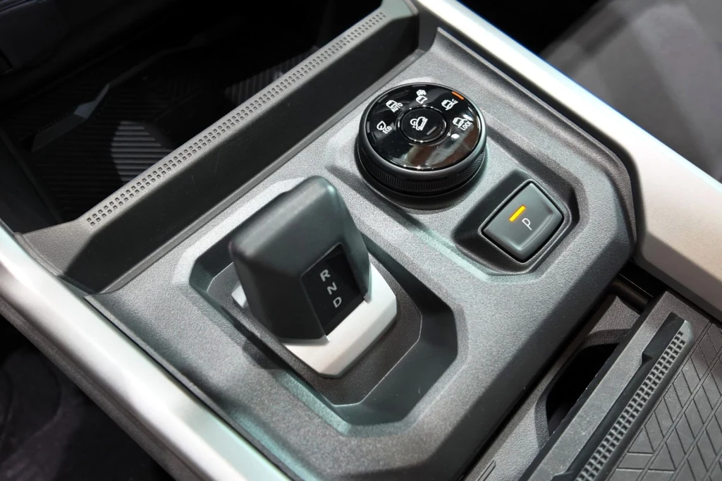 Trybami pracy układu napędowego można sterować za pomocą specjalnego pokrętła znajdującego się obok dźwigni zmiany biegów. Panel sterowania samochodu z widoczną dźwignią zmiany biegów automatycznych, pokrętłem do obsługi trybów jazdy oraz przyciskiem elektronicznego hamulca postojowego. Całość umieszczona w eleganckiej konsoli środkowej nowoczesnego wnętrza pojazdu.