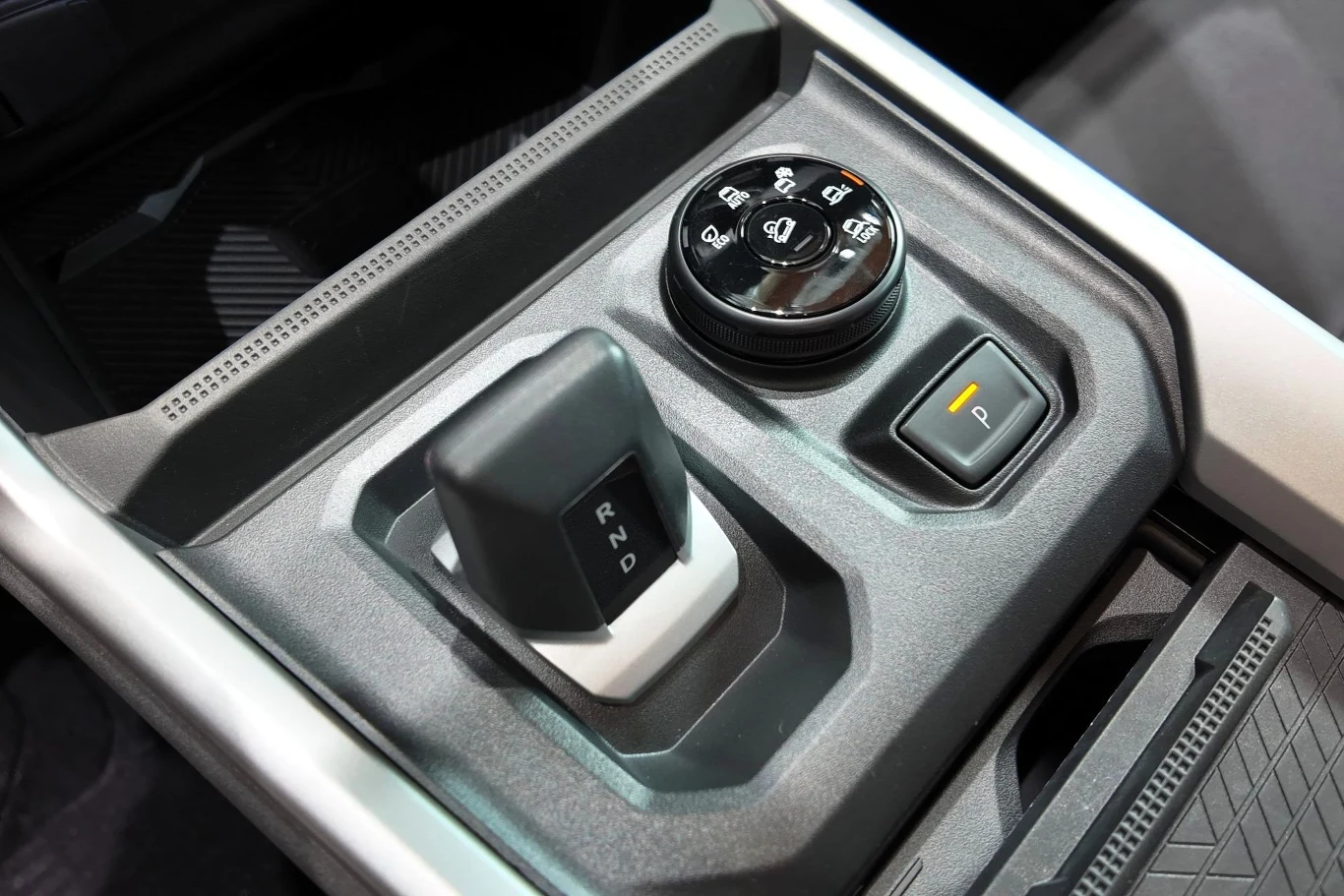 Panel sterowania samochodu z widoczną dźwignią zmiany biegów automatycznych, pokrętłem do obsługi trybów jazdy oraz przyciskiem elektronicznego hamulca postojowego. Całość umieszczona w eleganckiej konsoli środkowej nowoczesnego wnętrza pojazdu.