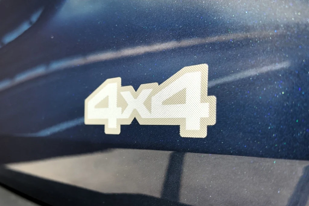 Dacia chwali się, że układ hybrid-G 150 4x4 to pierwsze takie rozwiązanie na świecie. Jasny emblemat z napisem 4x4 umieszczony na ciemnej powierzchni pojazdu wyróżnia się na tle metalicznej karoserii.