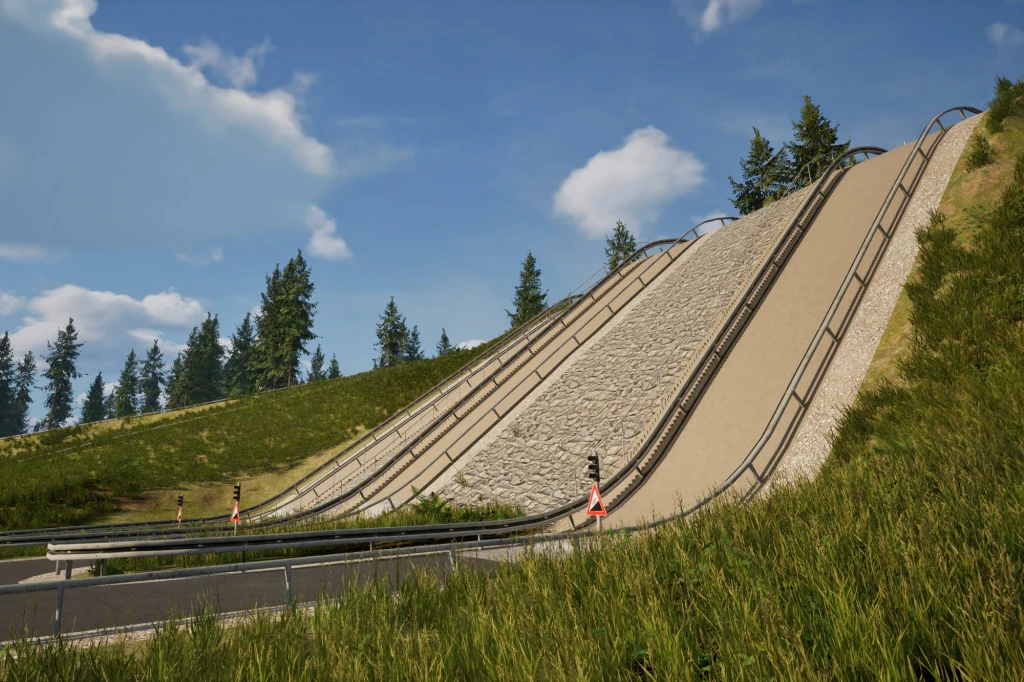 Pod najbardziej strome podjazdy w Immendingen wyjeżdżają tylko dwa pojazdy z gamy Mercedesa - klasa G oraz Unimog Skocznia narciarska otoczona zielonymi wzgórzami i drzewami, pokryta igelitową i piaszczystą nawierzchnią z metalowymi barierkami ochronnymi, poniżej biegnie droga asfaltowa.