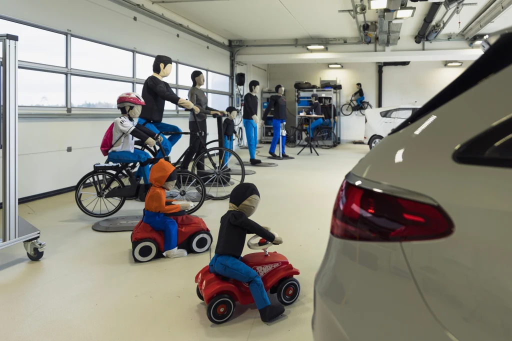 Cały zestaw poruszających się autonomicznie manekinów pozwala sprawdzać reakcję systemów bezpieczeństwa na wszystkich uczestników ruchu drogowego Wnętrze laboratorium testowego z manekinami symulującymi pieszych i rowerzystów oraz dziećmi na zabawkowych pojazdach, obok fragment pojazdu osobowego, całość służy testom bezpieczeństwa drogowego.