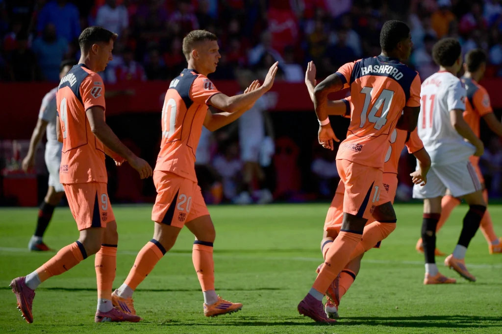 Piłkarze w pomarańczowych strojach świętują zdobycie bramki podczas meczu na stadionie, w tle widownia oraz rywale w białych koszulkach.