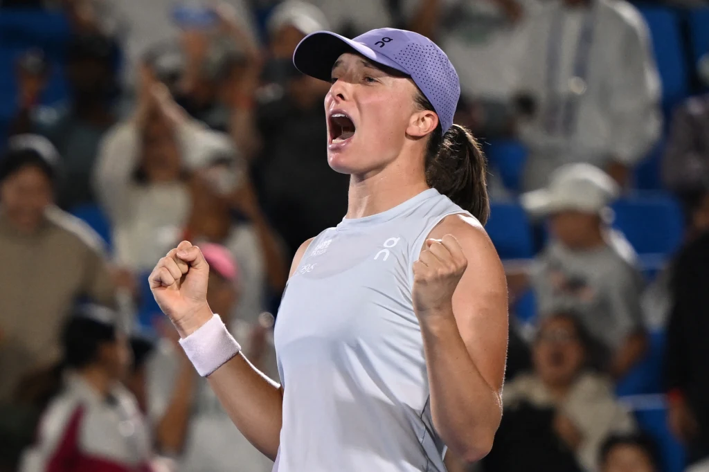 Zawodniczka tenisa wyrażająca radość i emocje po zwycięstwie, ubrana w sportowy strój, z zaciśniętymi pięściami, w tle widownia kibicująca uczestnikom meczu.