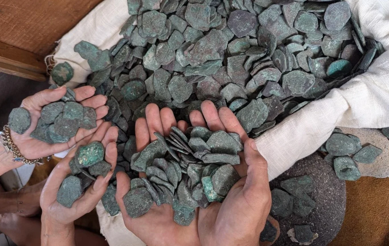 Nurkowie odkrywają ukryte bogactwa hiszpańskiego imperium. Ponad 1000 monet Ręce trzymające dużą ilość starych monet lub metalowych krążków, wysypanych z płóciennego worka, monety wydają się pokryte patyną, co sugeruje ich wiek i historyczną wartość.