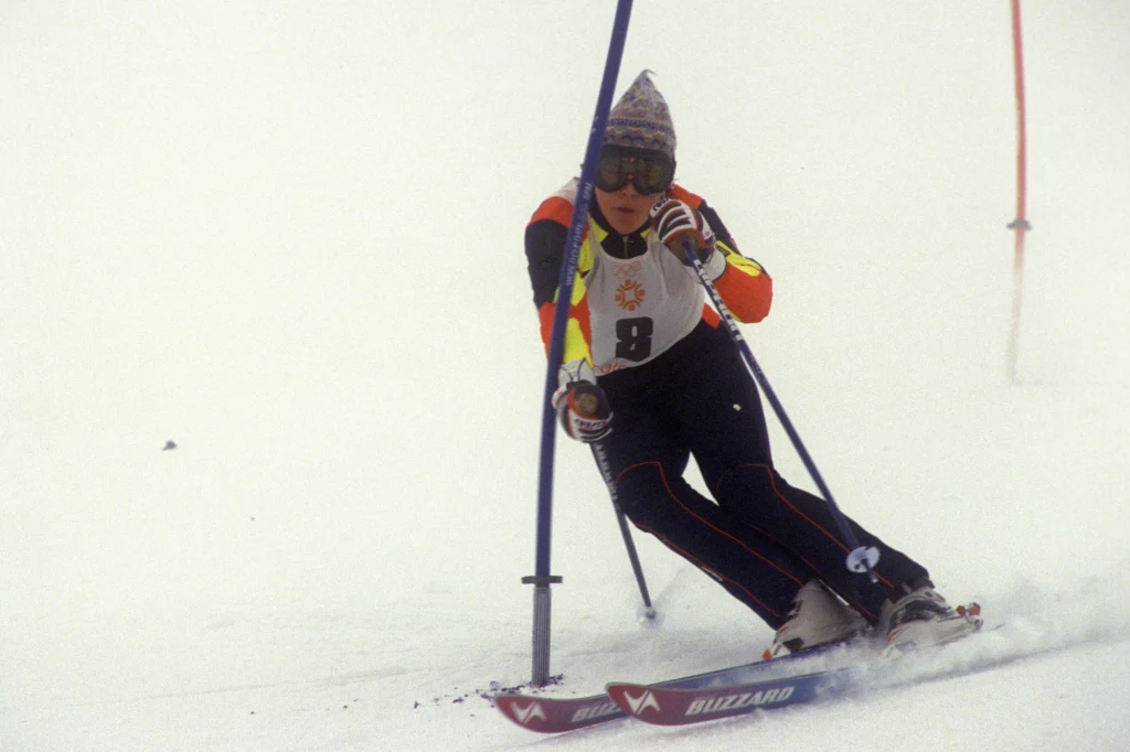 Dorota Tlałka na igrzyskach olimpijskich w Sarajewie Narciarz w sportowym kombinezonie i kasku z goglami pokonuje trasę slalomu, dynamicznie skręcając pomiędzy tyczkami na zaśnieżonym stoku.