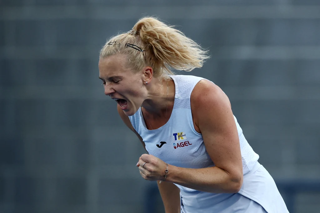 Kobieta w sportowym stroju tenisowym wyraża silne emocje, zaciskając pięść i krzycząc z triumfem na korcie tenisowym, tło rozmyte.