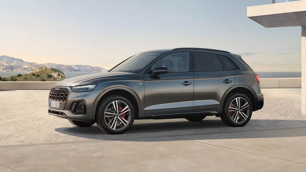 Program Audi Select :plus odmienia sytuację na rynku aut używanych Szary samochód typu SUV marki Audi zaparkowany na otwartej przestrzeni na tle gór i jasnego nieba, widoczny bok pojazdu, sportowe felgi oraz nowoczesna sylwetka.