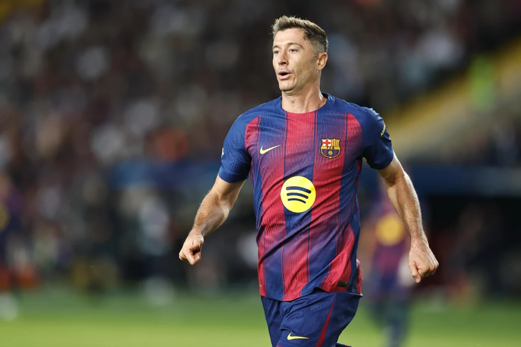 Piłkarz w stroju FC Barcelony biegnie po murawie stadionu podczas meczu, na jego koszulce widnieje logo sponsora, w tle rozmazana publiczność.