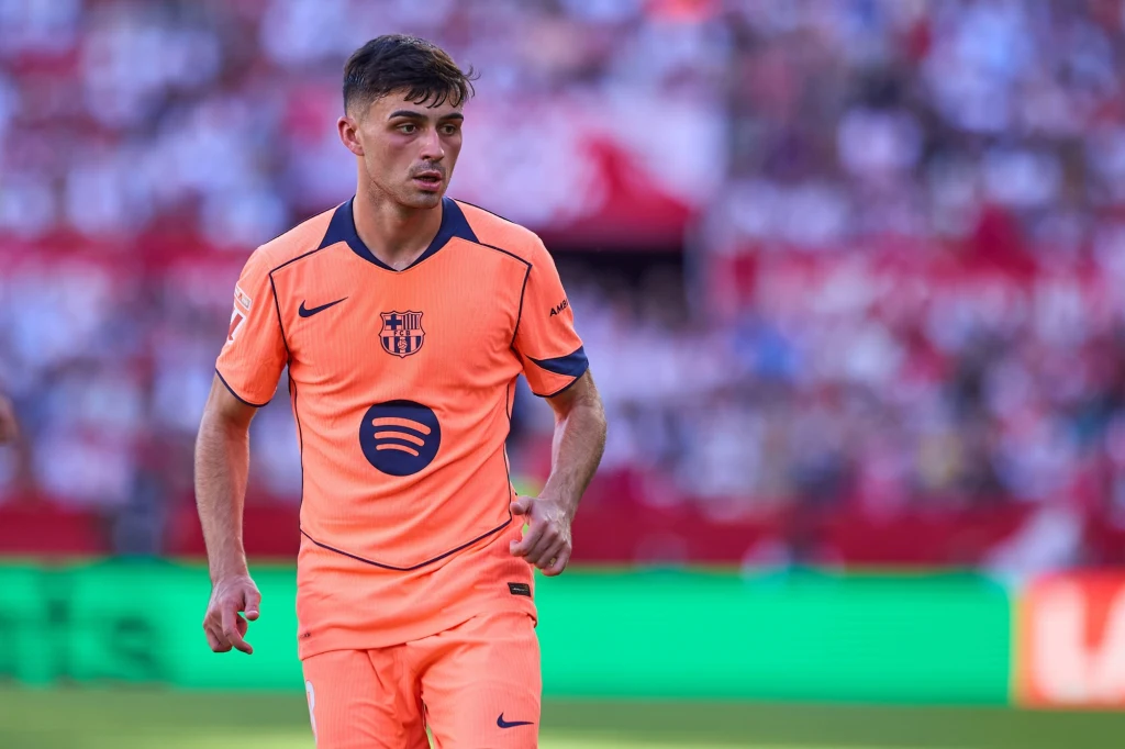 Piłkarz w pomarańczowym stroju FC Barcelony znajduje się na boisku w trakcie meczu, w tle rozmyta publiczność na trybunach.