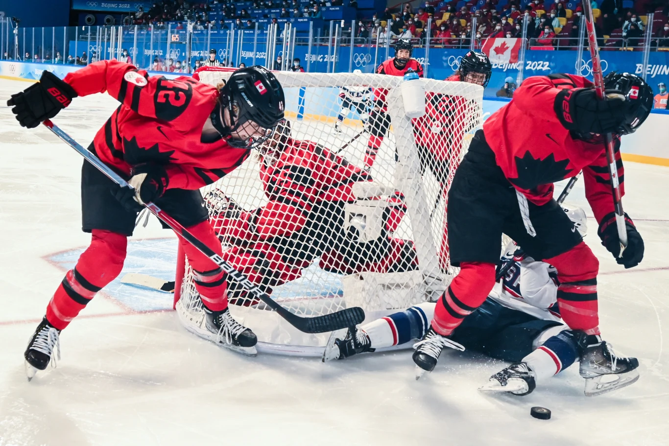 Złota z Pekinu w hokeju kobiet podczas zimowych igrzysk olimpijskich 2026 będzie broniła Kanada Dynamiczna akcja pod bramką podczas meczu hokeja na lodzie, zawodniczki w czerwonych strojach z liściem klonu bronią dostępu do bramki, a jedna z przeciwniczek leży na lodzie tuż przy słupku.