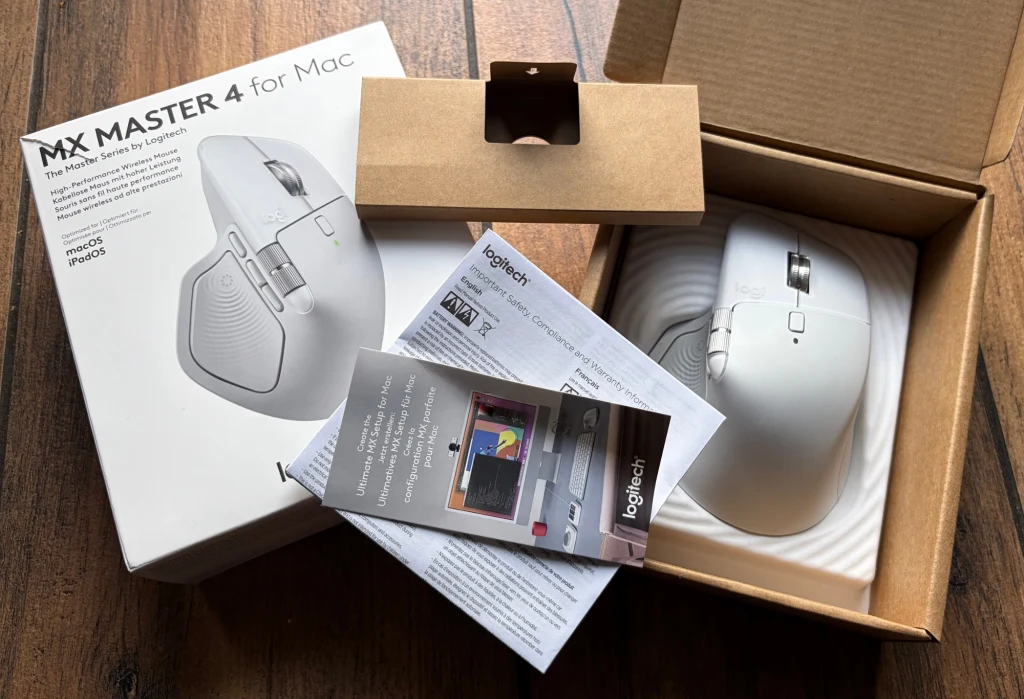 Zawartość opakowania z Logitech MX Master 4. Bezprzewodowa mysz komputerowa w jasnej wersji kolorystycznej wraz z oryginalnym opakowaniem, instrukcjami obsługi i kartą gwarancyjną, ułożona na drewnianej powierzchni.