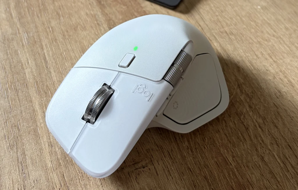Logitech MX Master 4 ma precyzyjne kółko MagSpeed. Biała mysz komputerowa Logitech MX Master 3 umieszczona na drewnianym blacie, widoczna rolka przewijania oraz przyciski boczne.