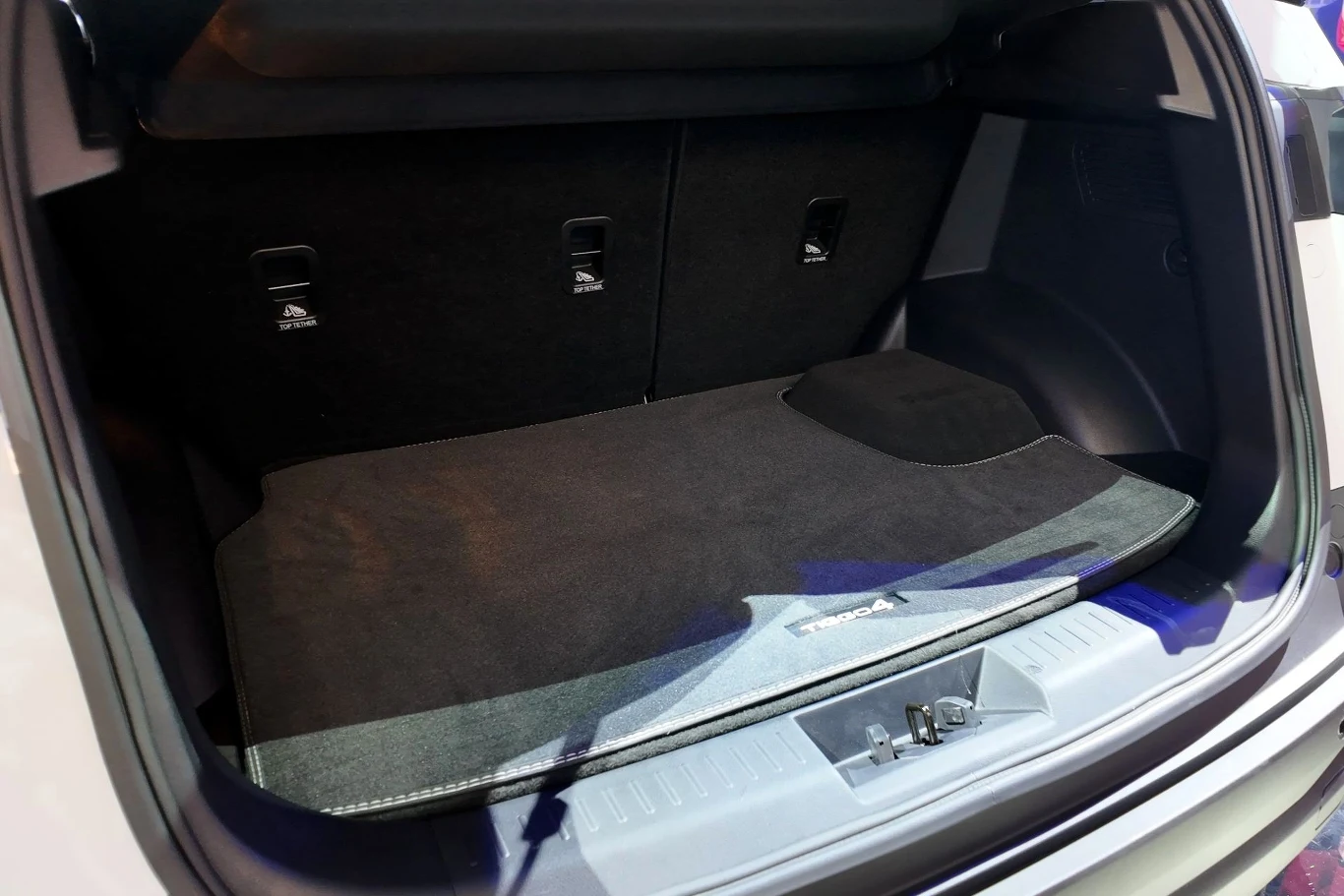 Bagażnik Chery Tiggo 4 HEV pomieści 430 litrów. Wystający element z podłogi ogranicza jednak funkcjonalność. Otwarty, pusty bagażnik samochodu wyłożony czarną wykładziną, z wyraźnie widocznymi zaczepami po bokach oraz schowkiem pod wykładziną.