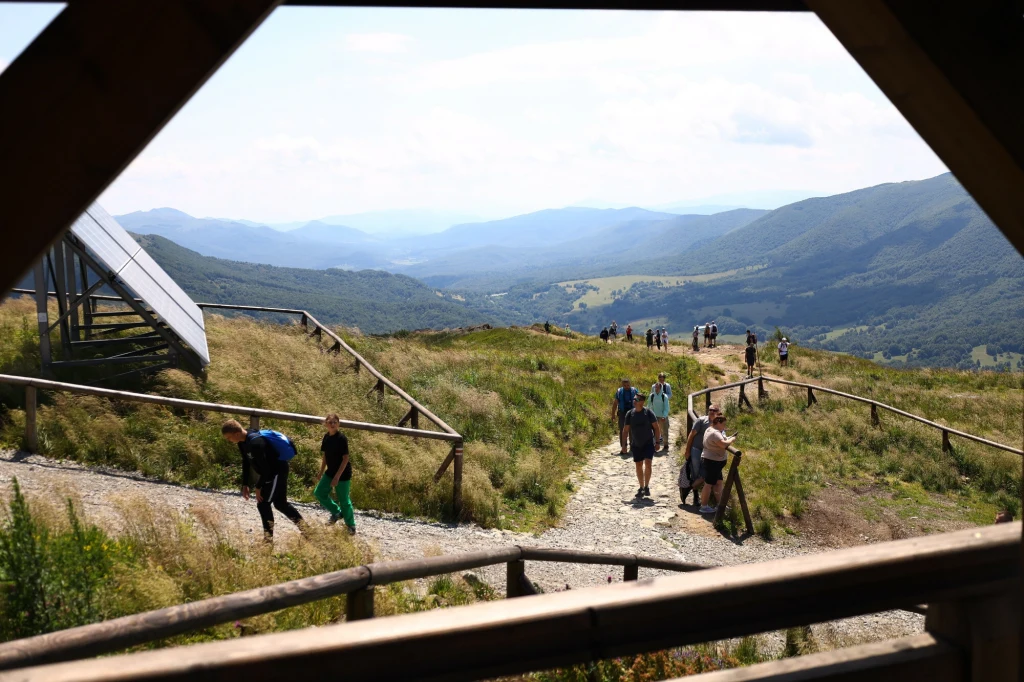 W dniu 11 listopada na Opołonek wejdzie tylko 150 osób Turyści spacerujący po górskim szlaku na tle rozległej panoramy górskiej z zielonymi wzgórzami i drewnianymi barierkami wzdłuż ścieżki.