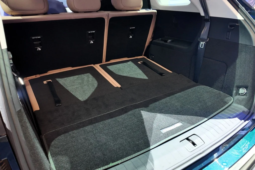 Przy złożonym trzecim rzędzie foteli bagażnik pomieści 819 litrów. Bagażnik samochodu z rozłożoną tylną kanapą tworzącą równą powierzchnię załadunkową, wyłożony czarną tapicerką, z widocznymi zagłówkami tylnej kanapy oraz jasnymi elementami wnętrza.