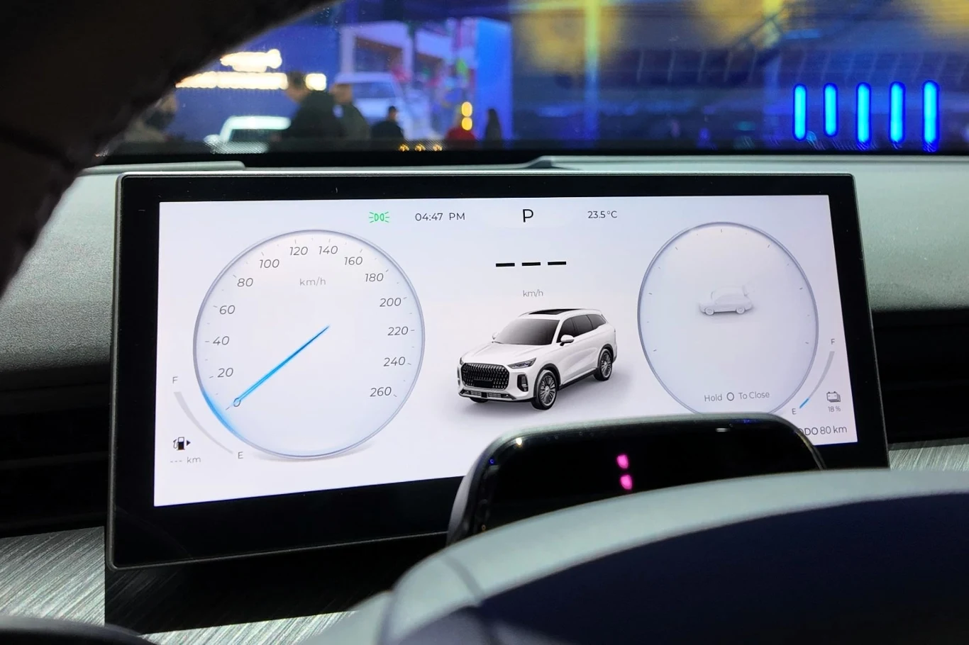 Nowoczesny cyfrowy kokpit samochodu z wyświetlaczem LCD, na którym widoczne są cyfrowe zegary, wskaźnik prędkości, temperatura zewnętrzna oraz graficzna prezentacja pojazdu pośrodku ekranu.