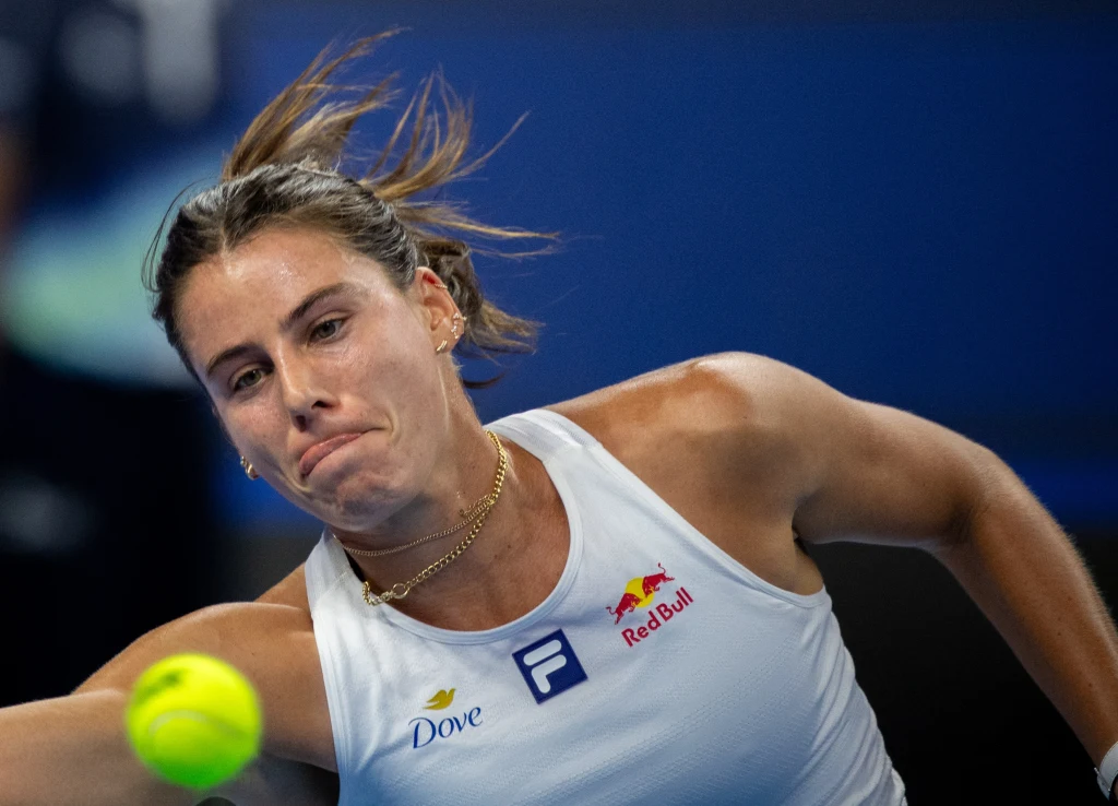 Emma Navarro Zbliżenie skoncentrowane na tenisistce podczas intensywnej wymiany piłki, wyraz determinacji na twarzy, widoczne logo sponsorów na stroju sportowym.