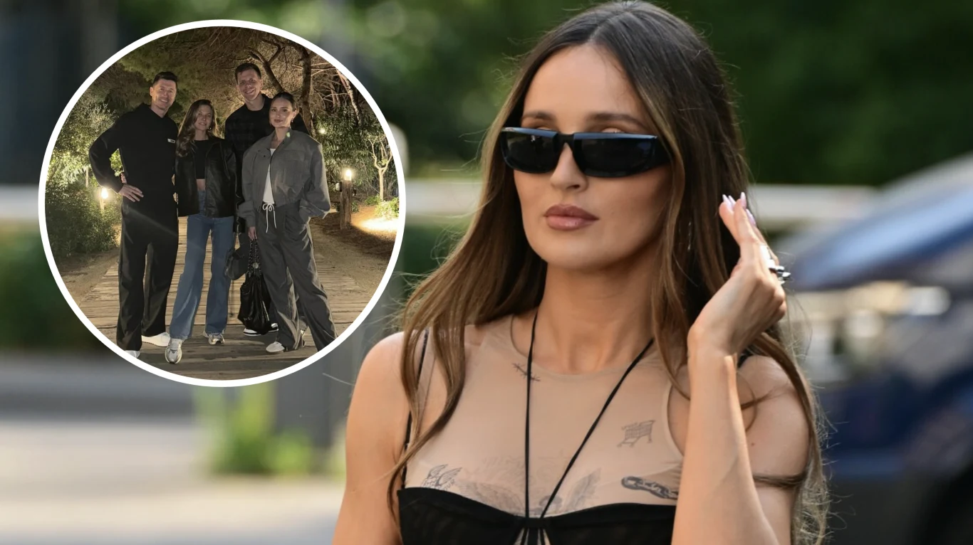 Kobieta w czarnych okularach przeciwsłonecznych, z długimi rozpuszczonymi włosami i tatuażami na klatce piersiowej, wystylizowana w modny sposób, stoi na zewnątrz. W lewym górnym rogu widoczne jest okrągłe wstawione zdjęcie przedstawiające cztery osoby...