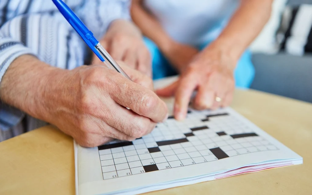 Krzyżówki wspierają pamięć oraz koncentrację Dwie osoby wspólnie rozwiązują krzyżówkę, jedna trzyma długopis i zapisuje odpowiedzi, druga wskazuje miejsce w krzyżówce palcem.