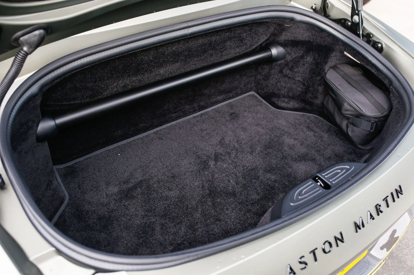 Bagażnik Astona Martina Vantage'a Roadstera pomieści 200 litrów. To o 150 litrów mniej niż w odmianie Coupe. Otwarty bagażnik samochodu z miękkim, czarnym wykładaniem, poprzeczka wzmacniająca oraz torba umieszczona po prawej stronie, na klapie widoczny napis ASTON MARTIN.
