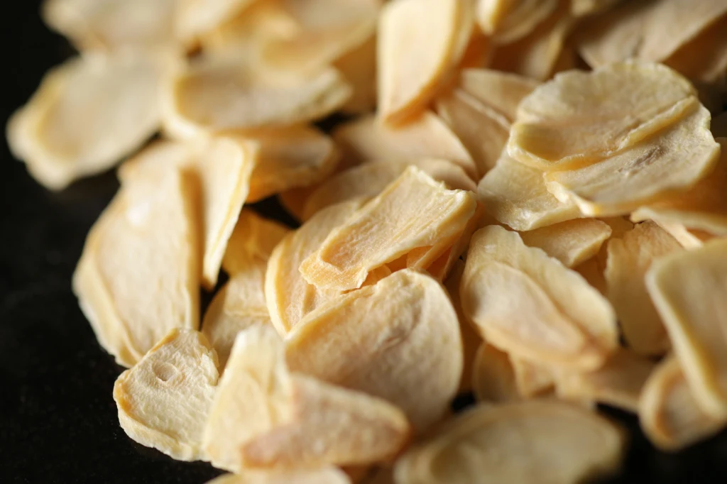 Pasternak nadaje się na chipsy Cienko pokrojone, wysuszone plasterki czosnku o jasnobeżowym kolorze, ułożone na ciemnym tle
