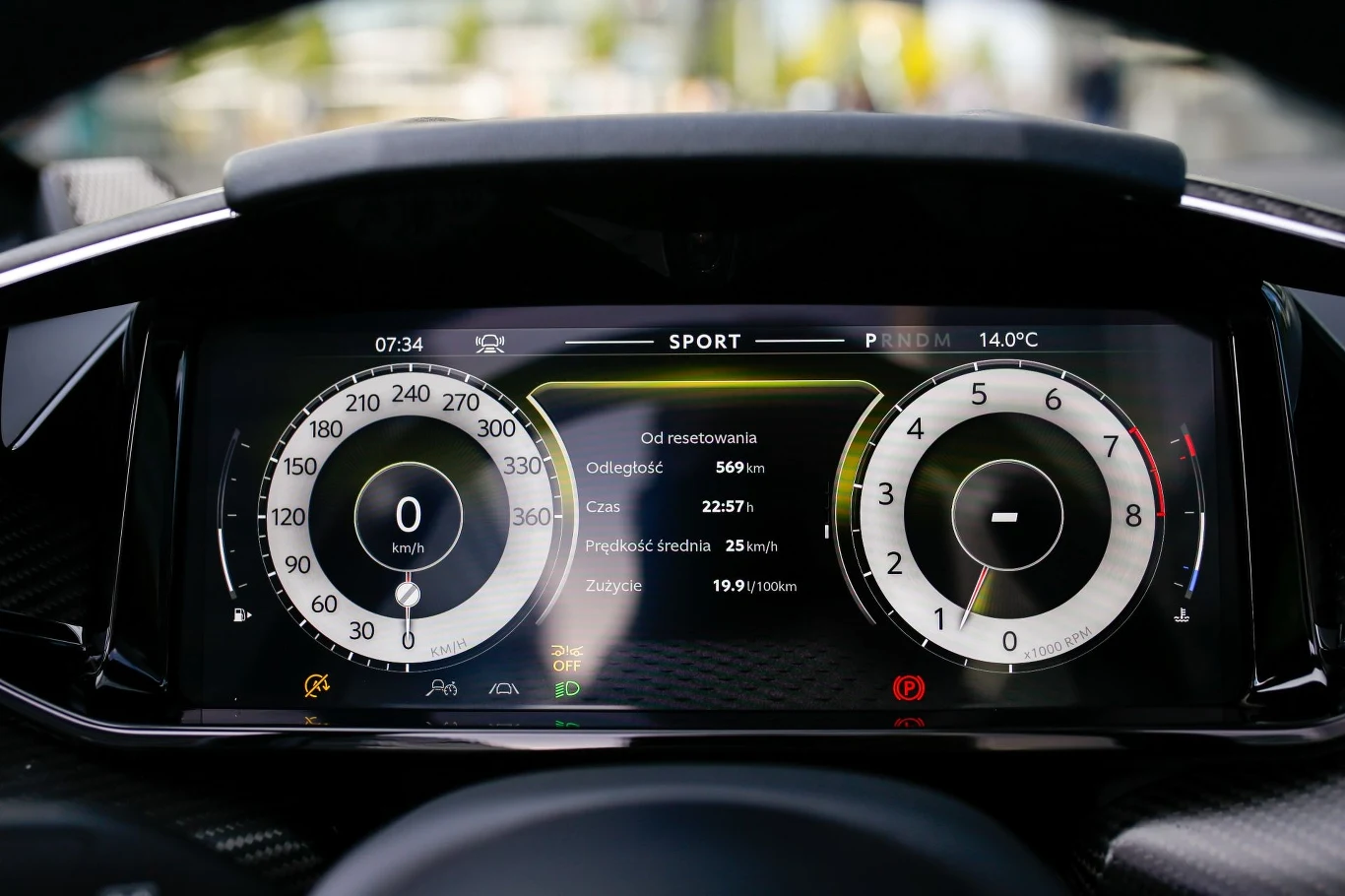 Konfigurowalny 10,25-calowy wyświetlacz wskaźników dostarcza wszelkich niezbędnych informacji. Cyfrowy wyświetlacz deski rozdzielczej samochodu prezentujący prędkościomierz, obrotomierz, wskazania podróżne oraz tryb jazdy sport. Tło rozmyte, dominują kontrastujące kolory wskaźników.