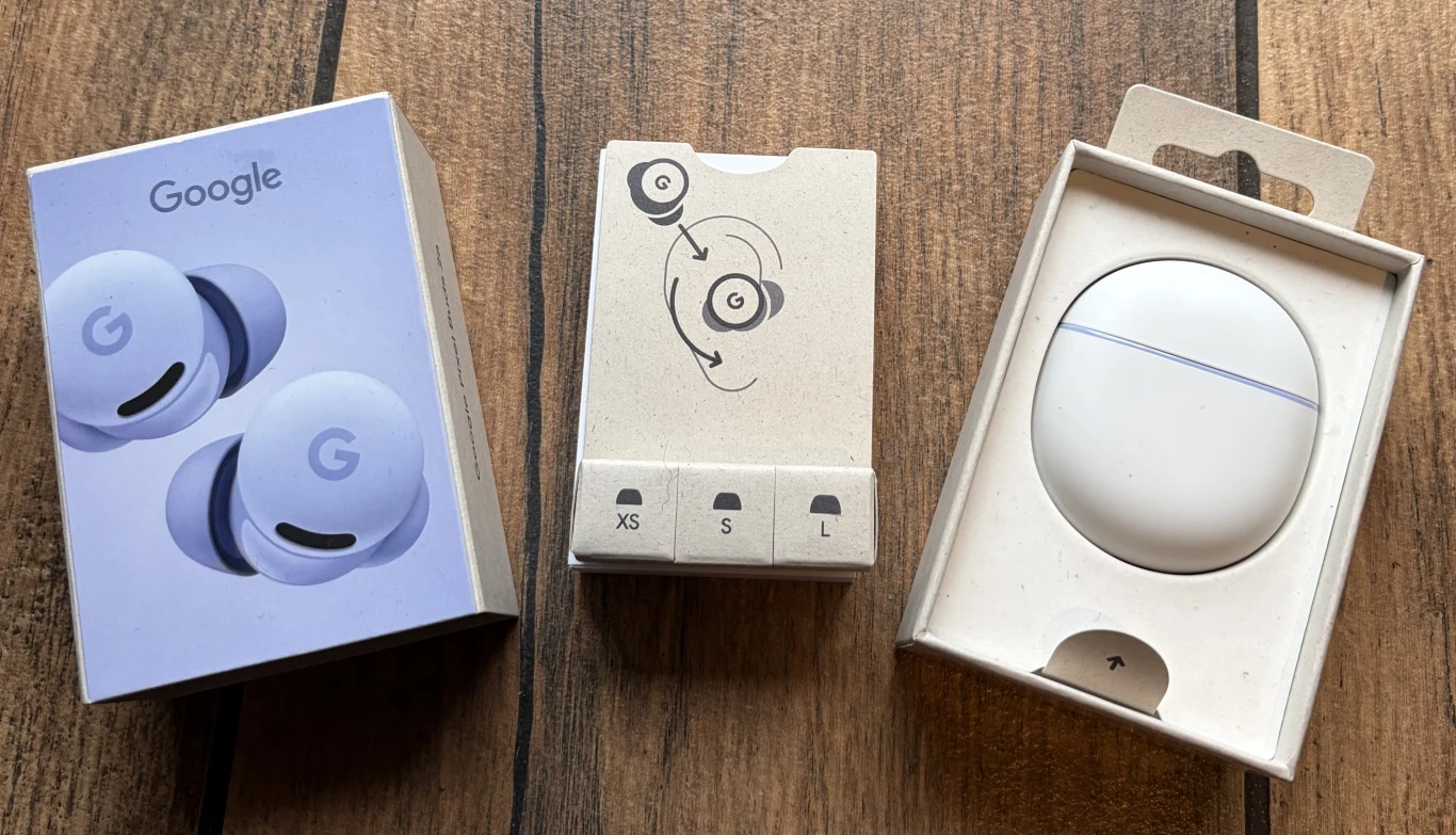 Zestaw słuchawek bezprzewodowych Google Pixel Buds w oryginalnym opakowaniu, pośrodku widoczny zestaw silikonowych końcówek dousznych w trzech rozmiarach, całość ustawiona na drewnianym tle.