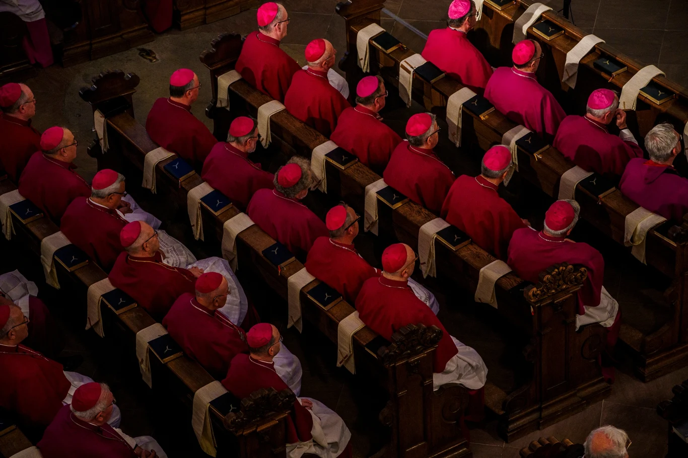 Europejscy biskupi apelują do Ursuli von der Leyen. "Pilna sprawa" Rzędy duchownych w purpurowych szatach i biretach siedzących w drewnianych ławach kościelnych podczas uroczystości lub zgromadzenia religijnego.
