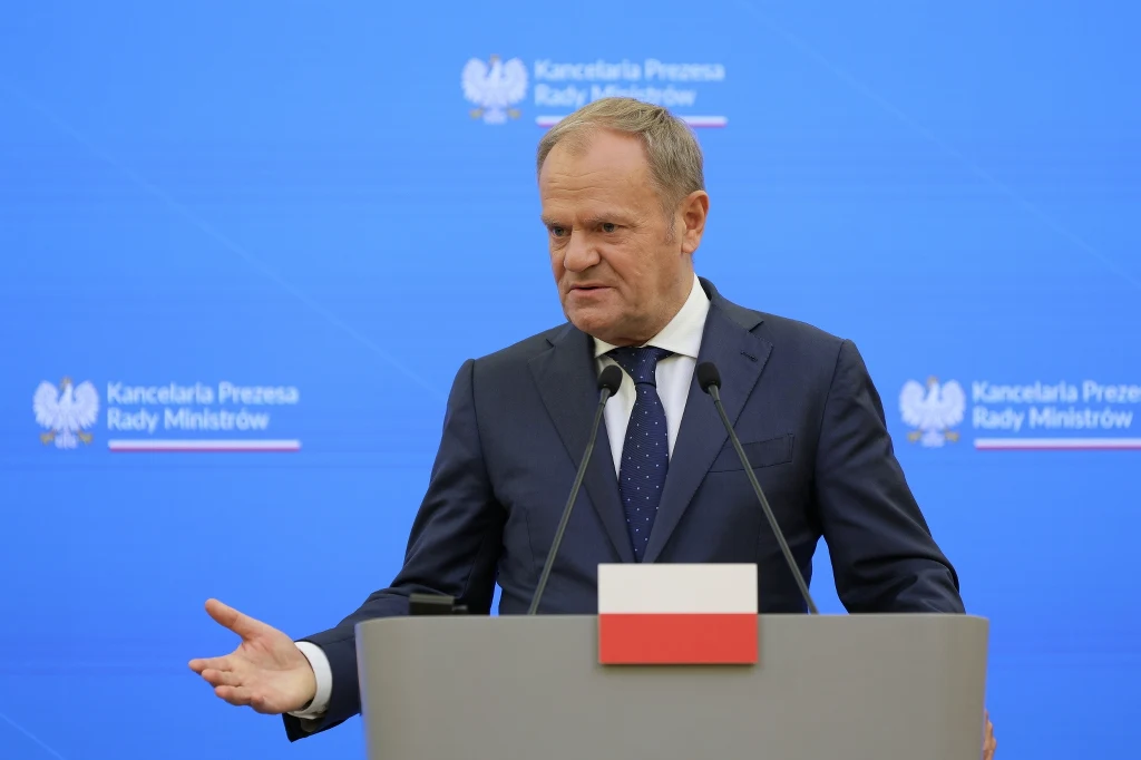Premier Donald Tusk na konferencji prasowej ze swoją litewską odpowiedniczką Ingą Ruginiene Mężczyzna w garniturze przemawia na konferencji prasowej, stojąc za mównicą z polską flagą i mikrofonami na tle niebieskiego ekranu z napisem 'Kancelaria Prezesa Rady Ministrów'.