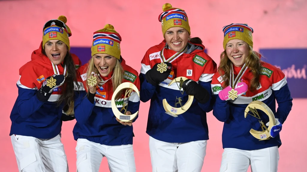 Cztery kobiety w norweskich strojach narodowych prezentujące złote medale i trofea, uśmiechnięte i pozujące do wspólnego zdjęcia po zwycięstwie sportowym.