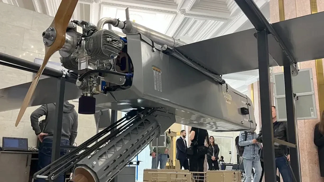 Ukraińcy ujawnili swoją tajną broń. To dron dalekiego zasięgu Fire Point FP-1 Duży dron wojskowy z widocznym silnikiem i śmigłem ustawiony na stojaku w pomieszczeniu, wokół kilka osób obserwujących urządzenie.