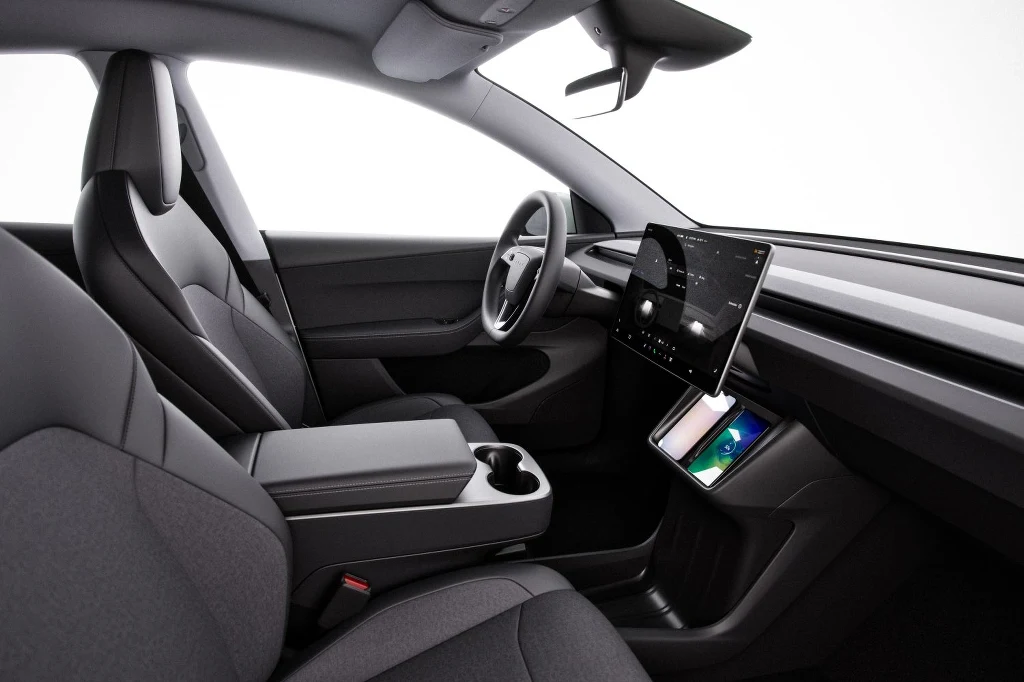 W uproszczonej wersji nie znajdziemy skórzanej tapicerki ani ambientowego podświetlenia Minimalistyczne wnętrze nowoczesnego samochodu z dużym centralnym ekranem dotykowym, wygodnymi fotelami w odcieniach szarości oraz uporządkowaną konsolą z uchwytami na kubki.