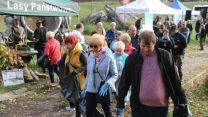 Grupa ludzi ubrana w ciepłą odzież bierze udział w akcji sprzątania terenu, trzymając worki na śmieci i rękawiczki ochronne, w tle namioty i baner Lasów Państwowych.
