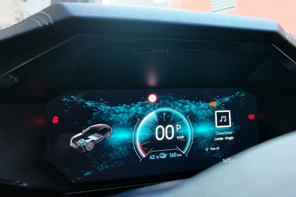Cyfrowy panel kokpitu samochodu prezentuje prędkościomierz, ikonę pojazdu, ostrzeżenia kontrolne, a także wyświetlacz muzyki z tytułem utworu i wykonawcą.