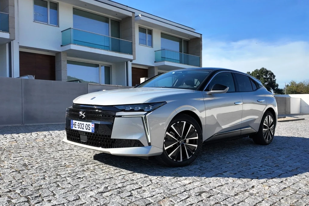 srebrny samochód osobowy nowoczesnej marki zaparkowany na brukowanym podjeździe, w tle nowoczesne apartamentowce z balkonami ze szklanymi balustradami