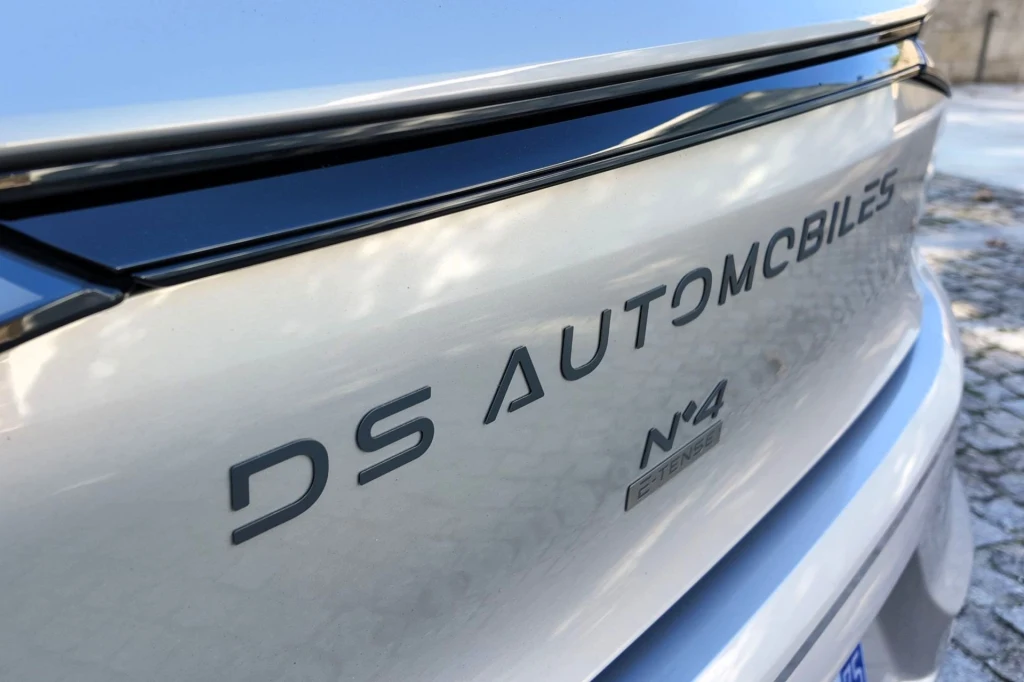 Błyszczący tył srebrnego samochodu marki DS Automobiles z wyraźnie widocznym logotypem i oznaczeniem modelu N°4 E-TENSE, fragment czarnej krawędzi klapy bagażnika oraz brukowana nawierzchnia w tle.
