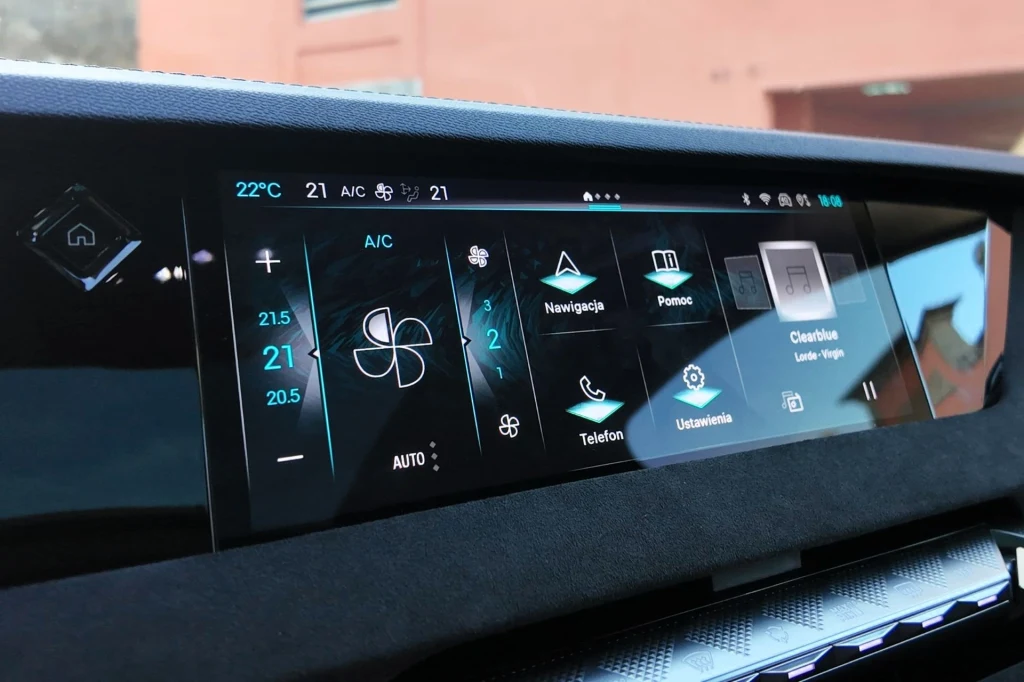 Panel dotykowy systemu multimedialnego w samochodzie, z widocznymi ikonami nawigacji, ustawień klimatyzacji, telefonu oraz innych funkcji pojazdu, pokazuje nowoczesny, cyfrowy interfejs kierowcy.