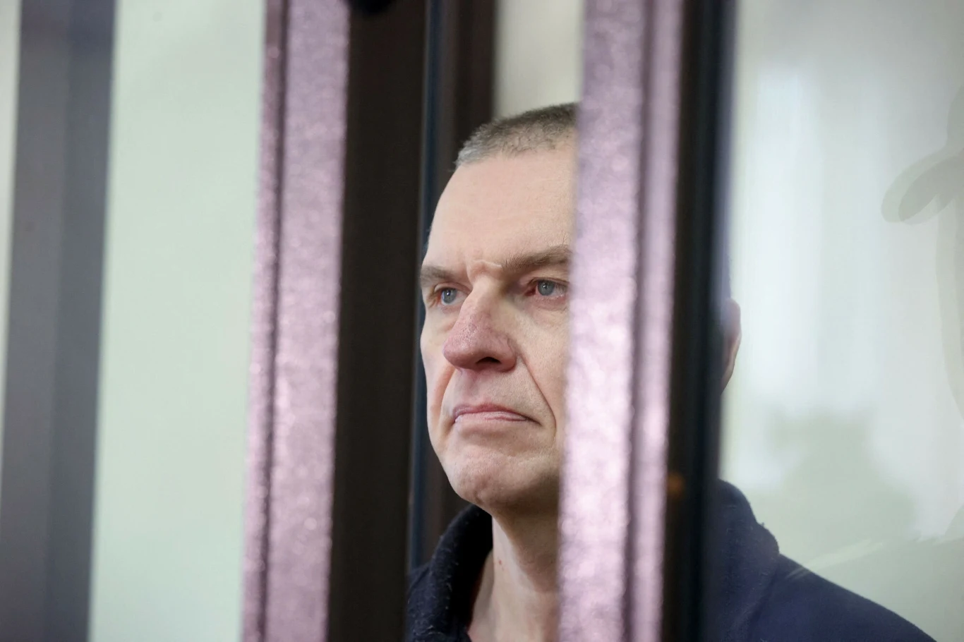 Andrzej Poczobut został ponownie osadzony w odizolowanej celi Mężczyzna o poważnym wyrazie twarzy stoi za szklaną przegrodą, patrząc przed siebie, ujęty w średnim planie, z wyraźnymi detalami mimiki.