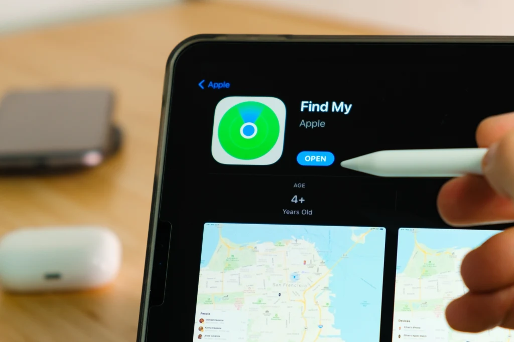 Funkcja Find My na iPhone może pomóc w sytuacji zgubienia lub kradzieży urządzenia Ekran tabletu wyświetlający aplikację Find My od Apple ze stylusem zbliżonym do ekranu oraz fragmentem słuchawek bezprzewodowych leżących w tle.