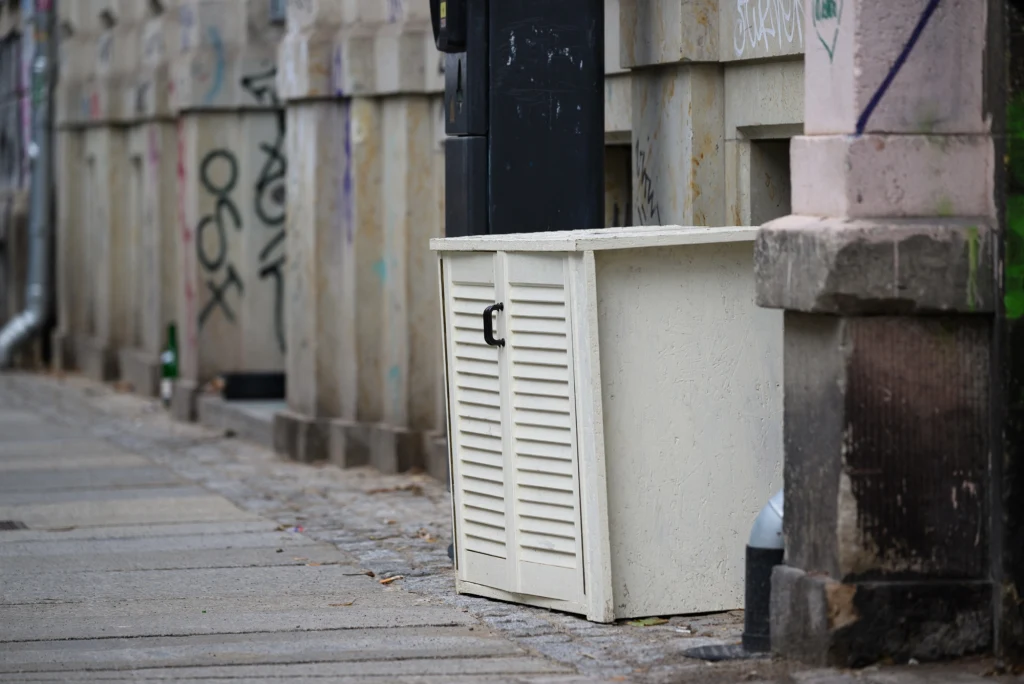 Nie tylko w Niemczech można znaleźć sporo mebli na ulicy Biała metalowa skrzynka ustawiona na chodniku przy ścianie budynku, z widocznymi graffiti oraz betonowymi elementami architektury miejskiej w tle.