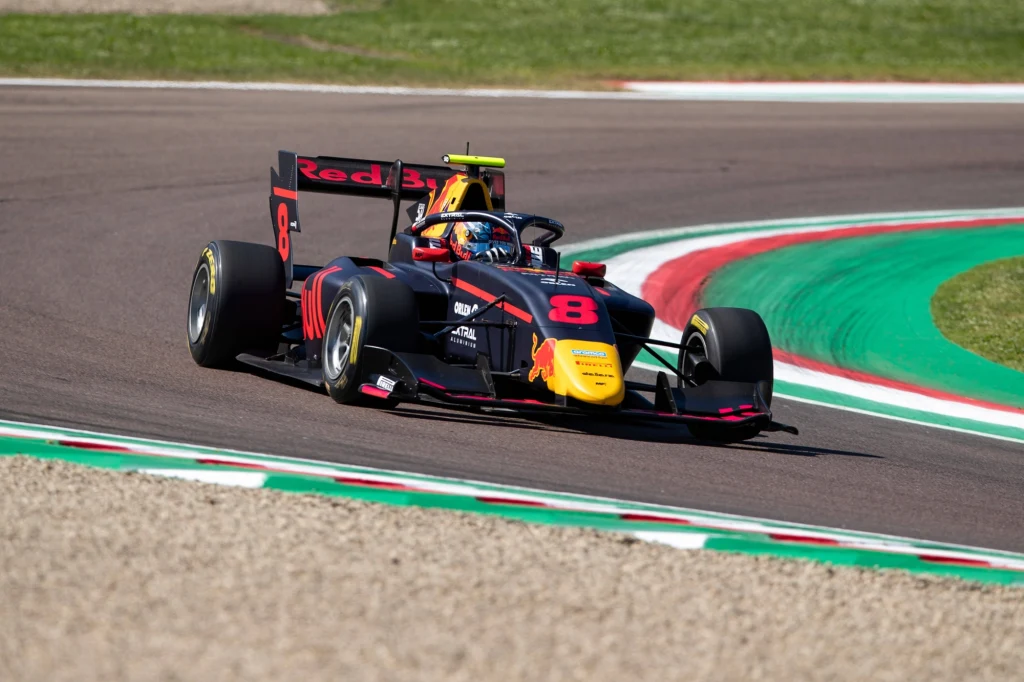 Kacper Sztuka Czarny bolid wyścigowy z wyraźnym numerem 8 i czerwonymi akcentami pokonuje zakręt na torze wyścigowym, w tle zielono-czerwone pasy oznaczające obrzeża asfaltu